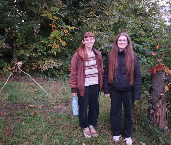 zwei junge Frauen stehen am Waldrand zwischen zwei selbst gemachten Naturkunstwerken