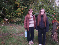 zwei junge Frauen stehen am Waldrand zwischen zwei selbst gemachten Naturkunstwerken