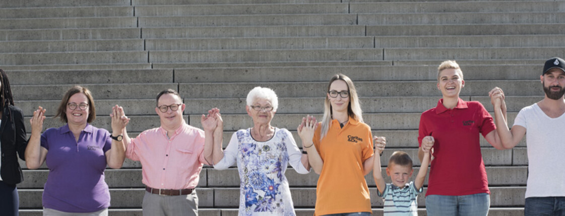 Zehn Menschen - verschiedenen Alters, Herkunft und Geschlecht stehen nebeneinander und geben sich die Hand.