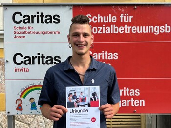 Junger Mann lächelt und hält eine Urkunde in die Kamera.